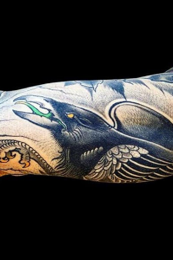Tattoo with a flying crow on the biceps